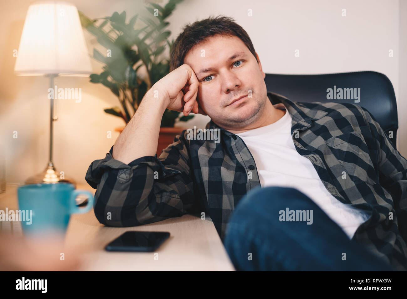 Ritratto di un giovane uomo informale che pongono nel suo ufficio di casa, guardando la telecamera. Foto Stock