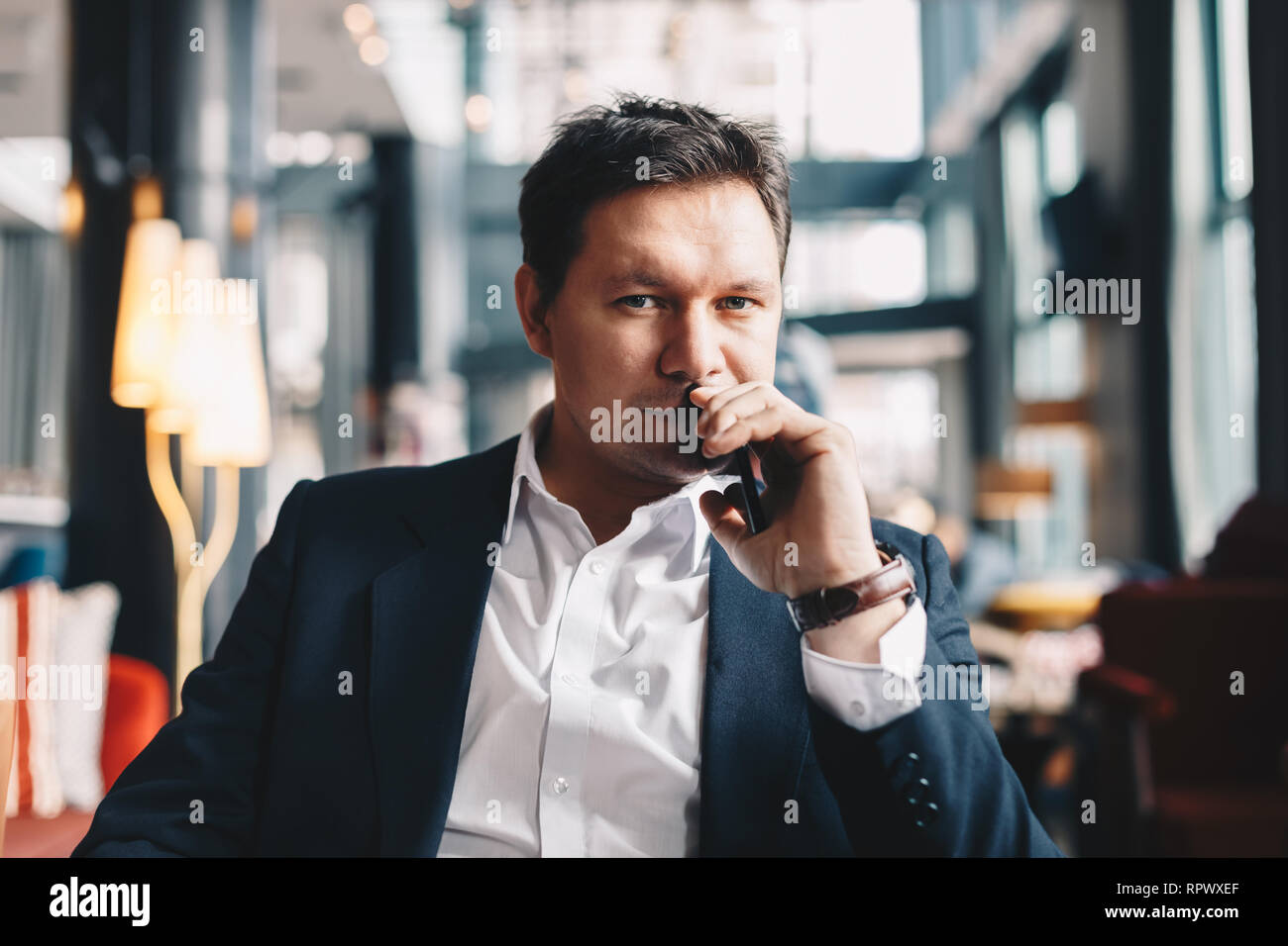 Close-up verticale della moderna giovane imprenditore con elevato livello di fiducia, seduto in un bar, in posa per la fotocamera. Foto Stock