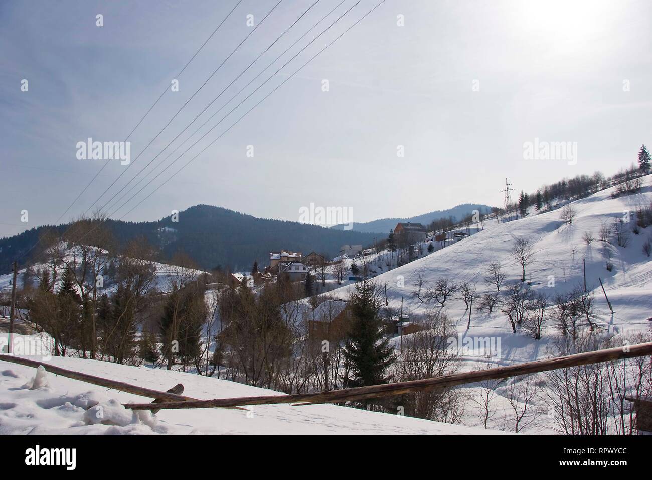 Giornata di sole, vista dalla finestra su un paesaggio innevato. Villaggio di montagna, case e recinzioni in Ucraina dei Carpazi. Foto Stock