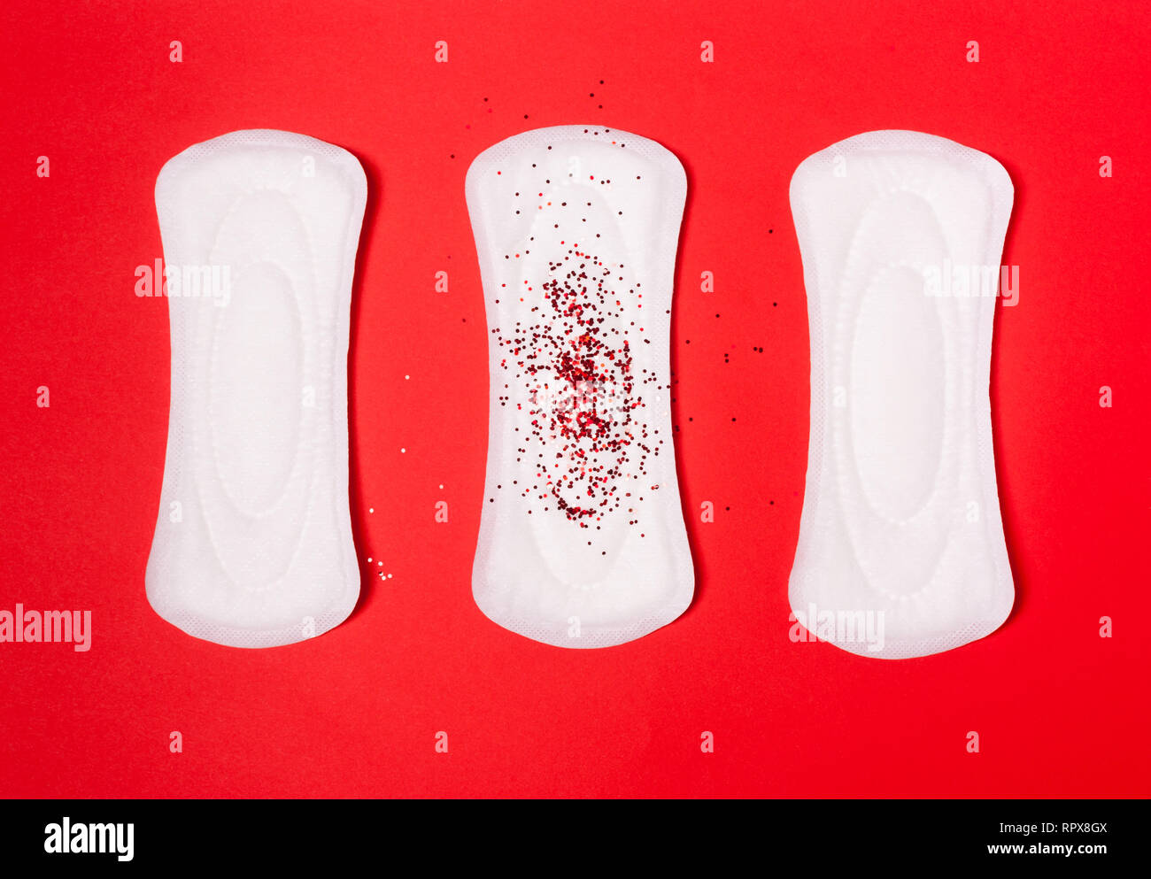 Tre assorbenti igienici su un corallo rosso sfondo. Il concetto di giorni critici, mestruazioni, donna ciclo periodico. Foto Stock