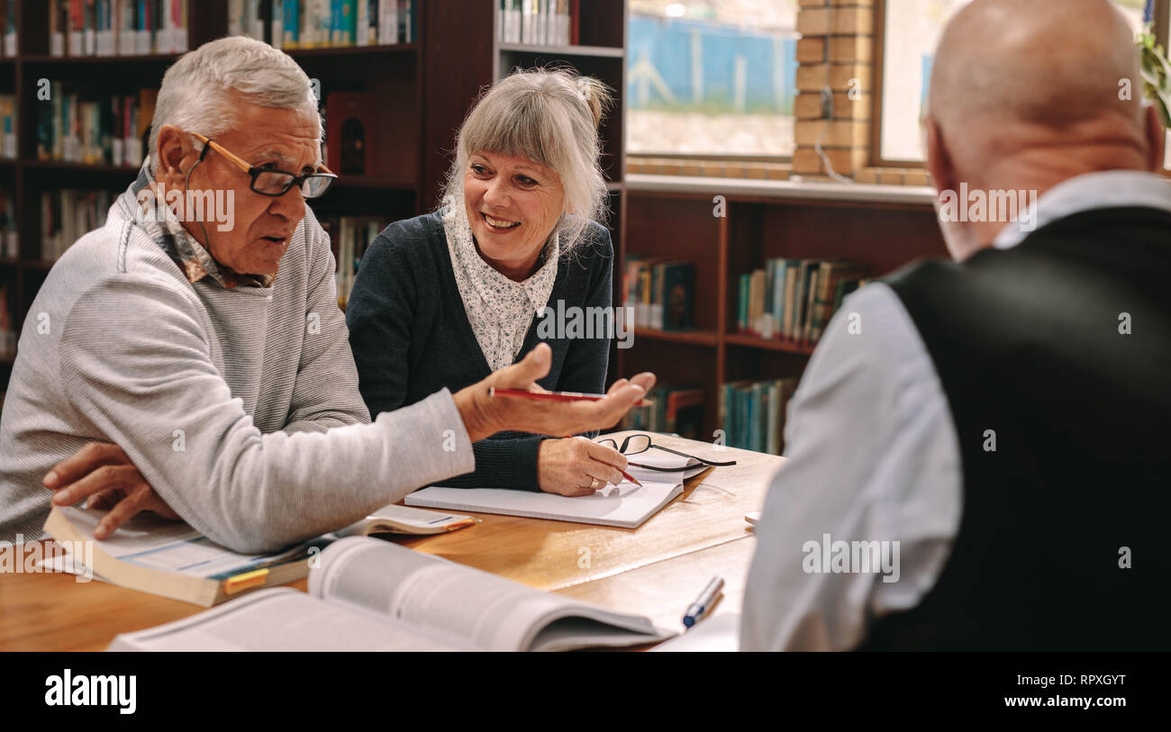 Due alti uomini e una donna seduta in una biblioteca con i libri di corso sul tavolo e discutere. Senior uomini e una donna di condividere idee e discutere di oggetto Foto Stock