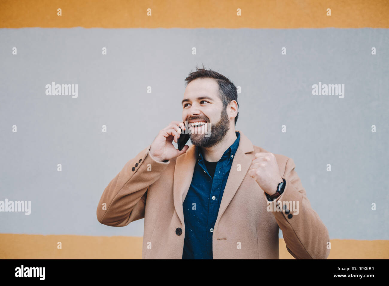 Ritratto di attraente e felice giovane maschio clenching freelance di suo pugno nel mezzo di una conversazione telefonica, celebrando la buona novella che egli ricevere Foto Stock