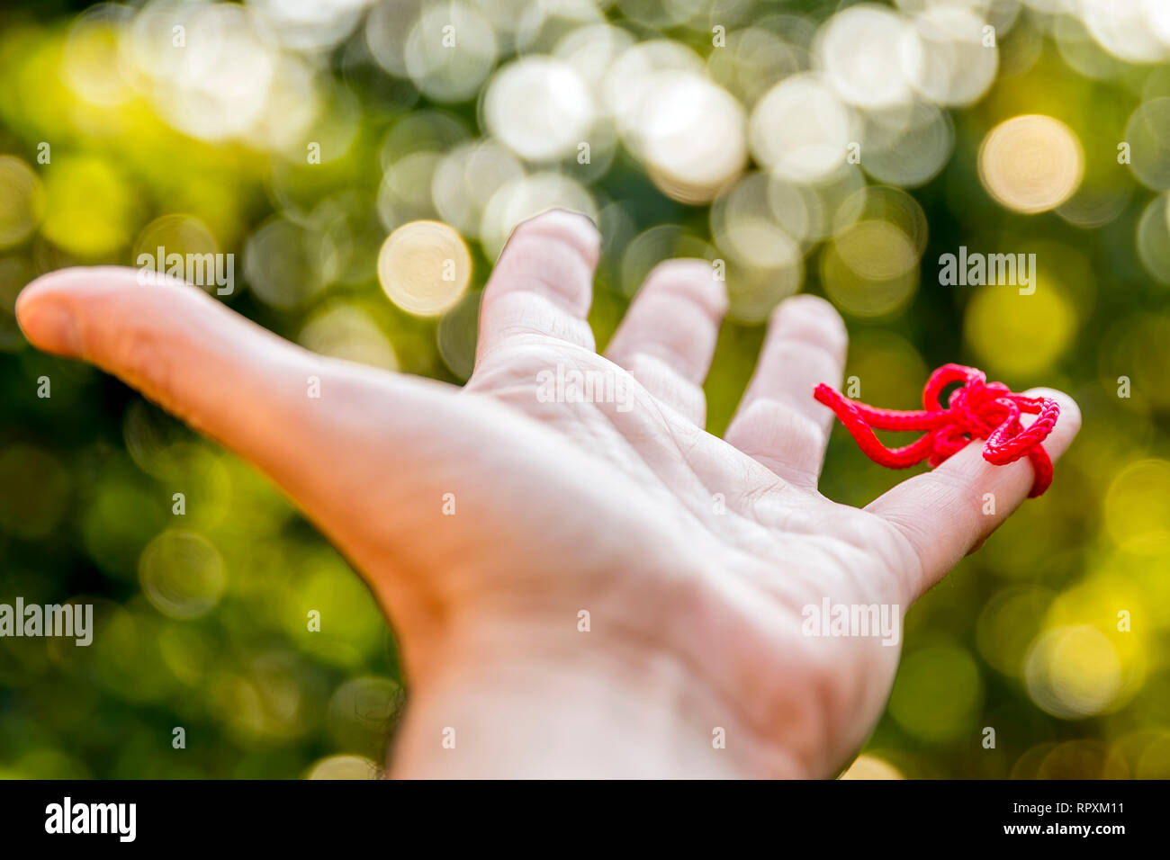 Filo rosso del destino legato al mignolo della mano sinistra contro un bellissimo sfondo bokeh di fondo Foto Stock