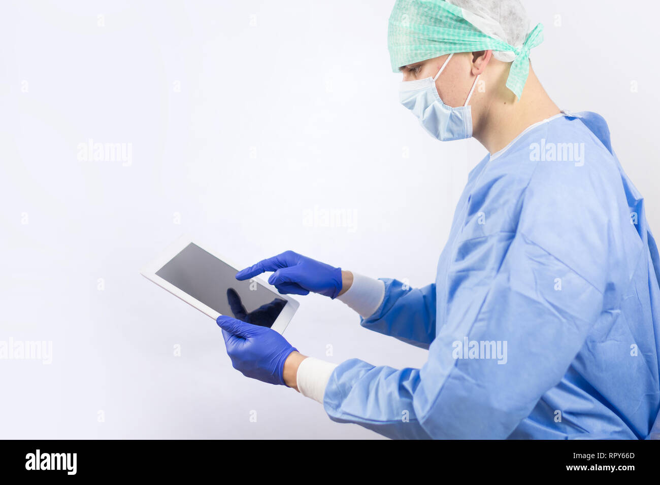 Medico chirurgo in guanti sterili preparando per il funzionamento utilizzando computer tablet. Indossa il cappuccio chirurgico e abito blu Foto Stock