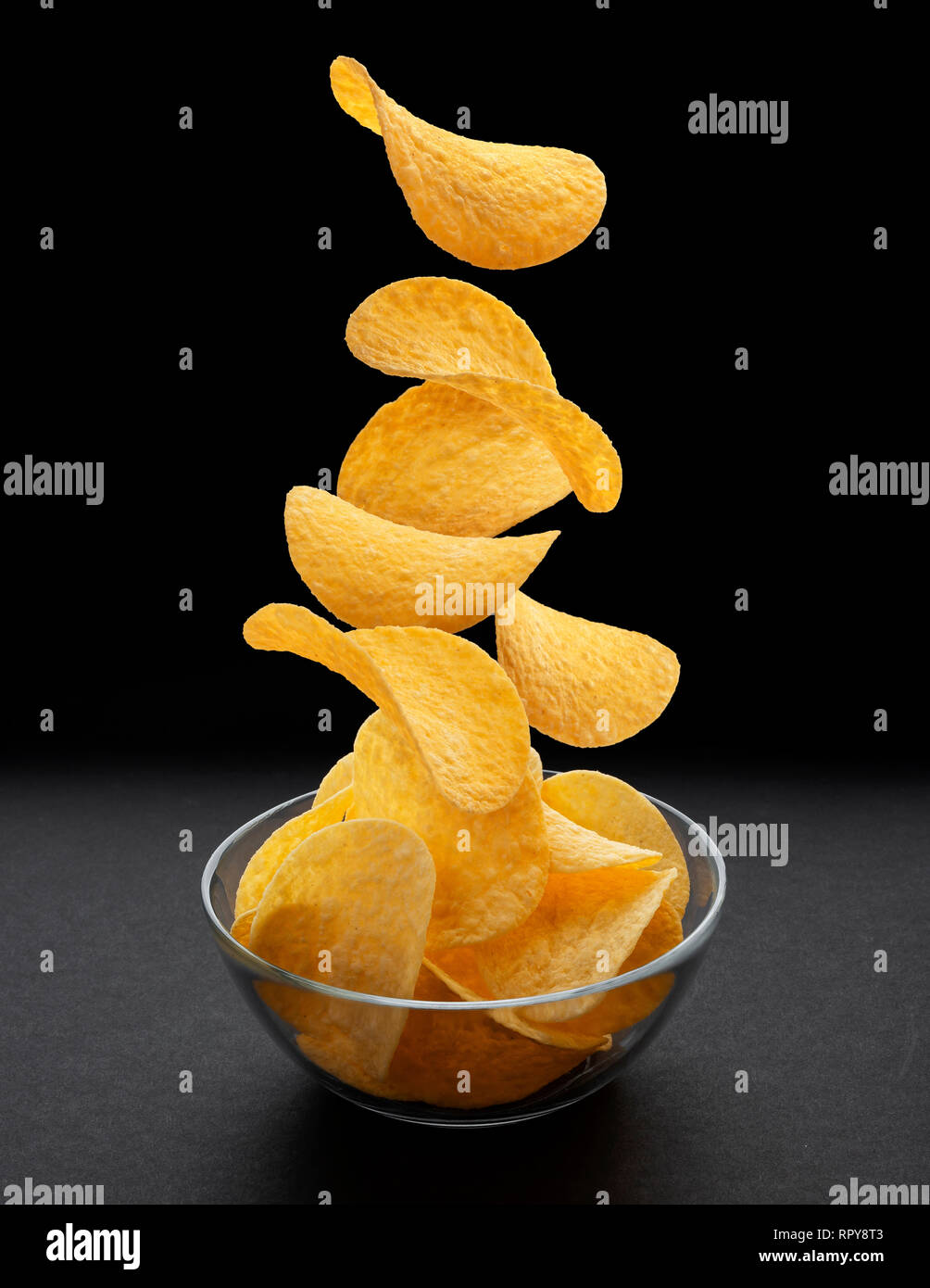 Potato chips di cadere nella ciotola di vetro su sfondo nero Foto Stock