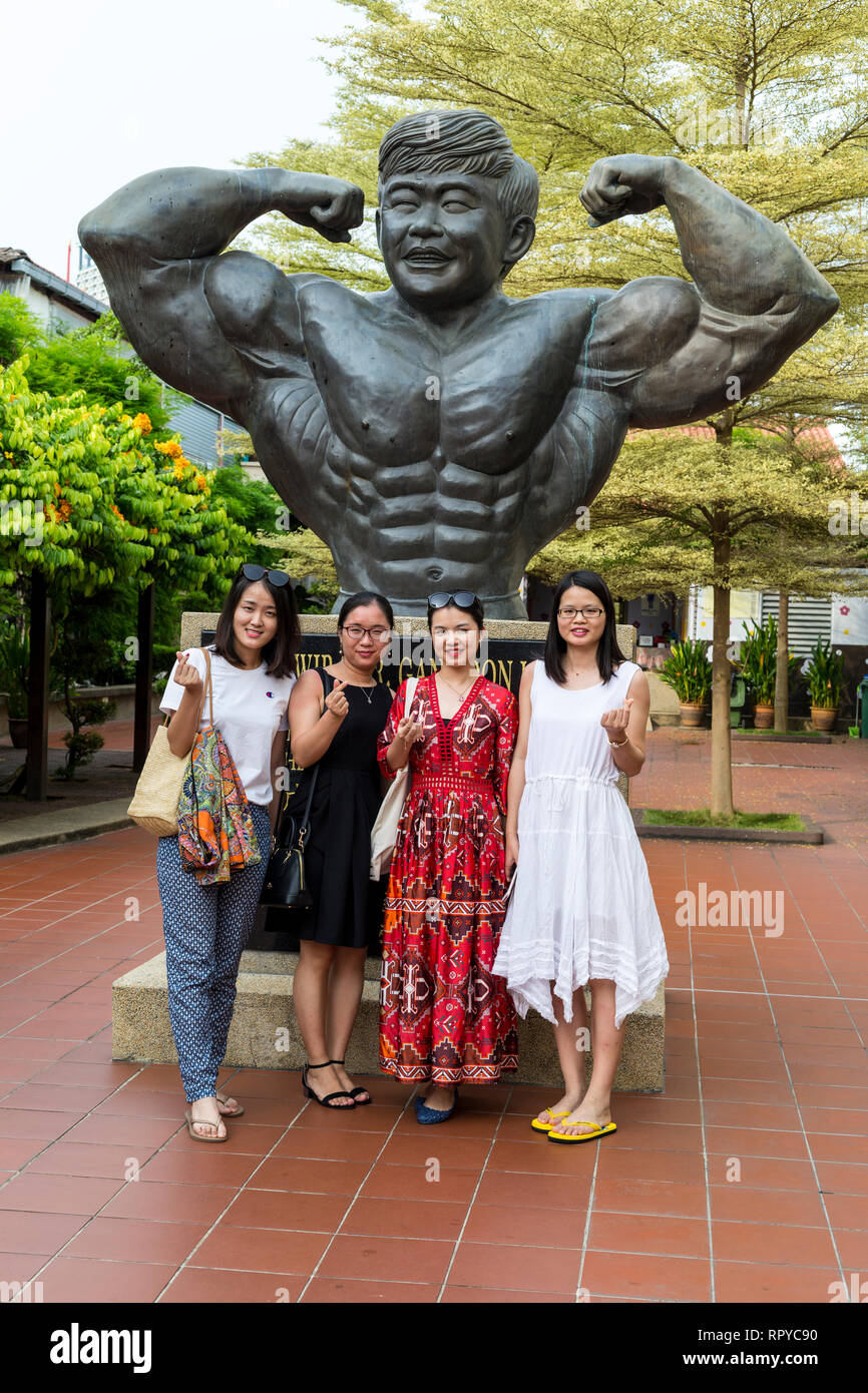 Il Gan Boon Leong statua, padre di Bodybuilding Malese, e le donne cinesi turisti, Melaka, Malaysia. Foto Stock