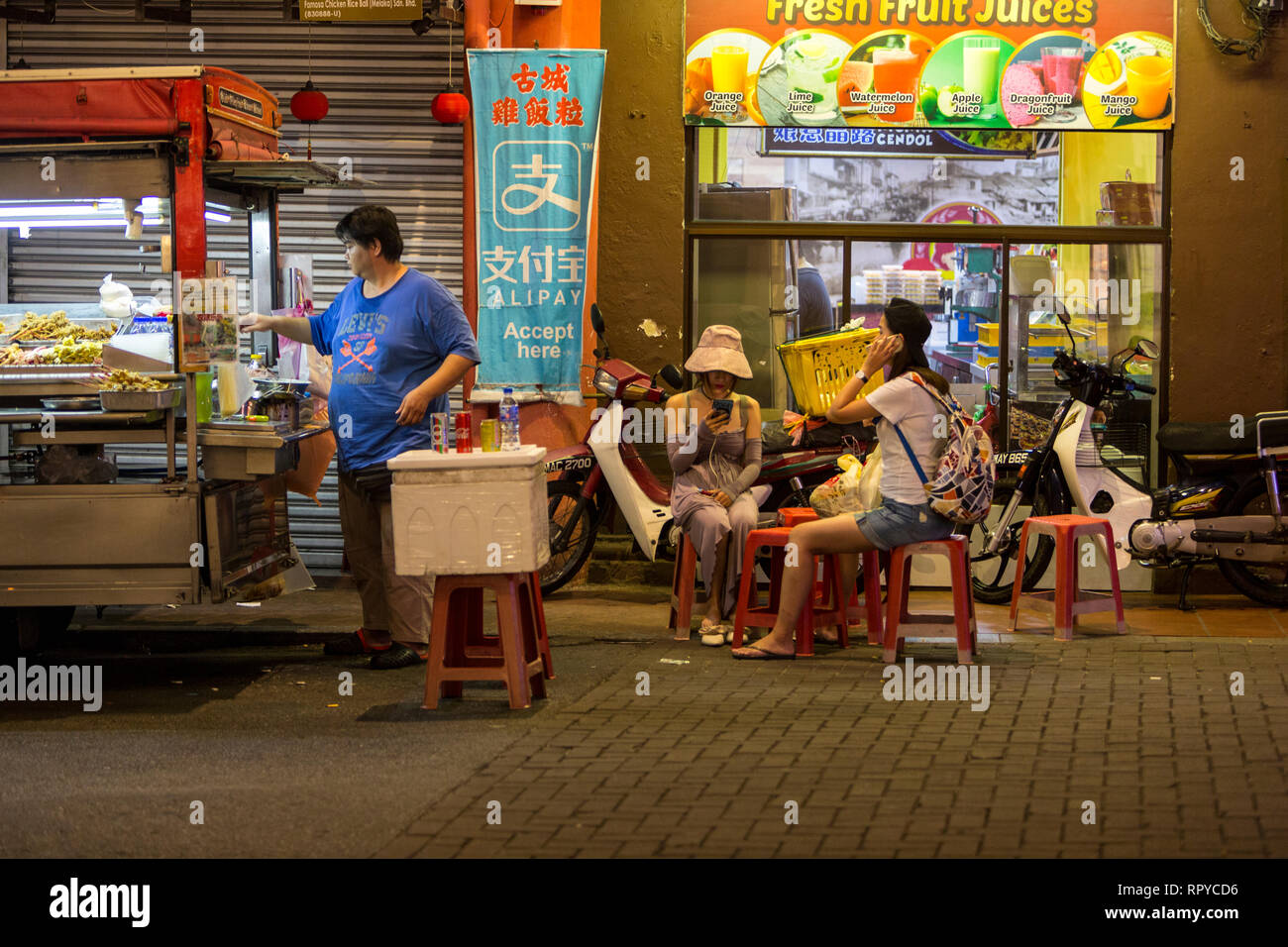 Cucina di strada venditore tende riposare mentre i turisti controllare i loro telefoni cellulari. Malacca, Malaysia. Foto Stock