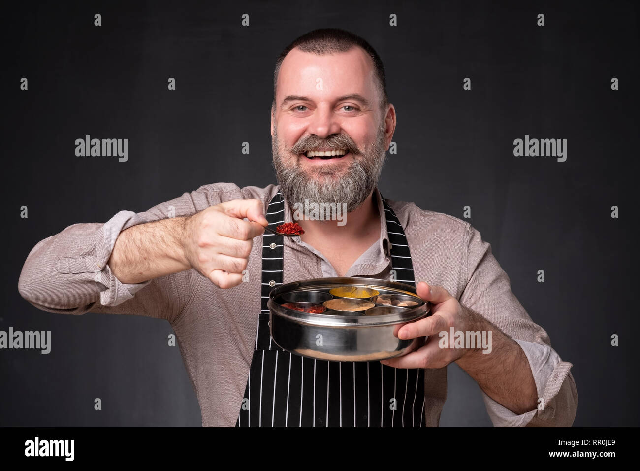 Maschio barbuto chef che mostra diverse spezie che egli utilizza. Segreto del cibo delizioso. Foto Stock