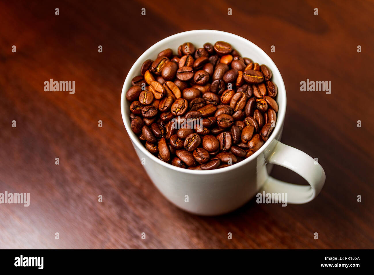 Chicchi di caffè tostati in un bianco mug tazza isolata su una tavola in legno rustico Foto Stock