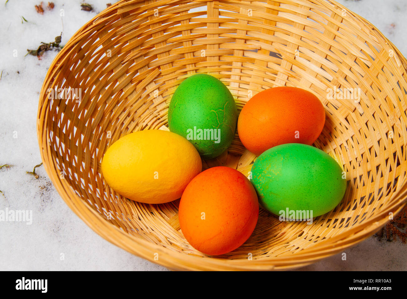 Cinque colorate uova di pasqua in un cesto di paglia sulla sommità di neve ed erba isolato caccia all'uovo Foto Stock