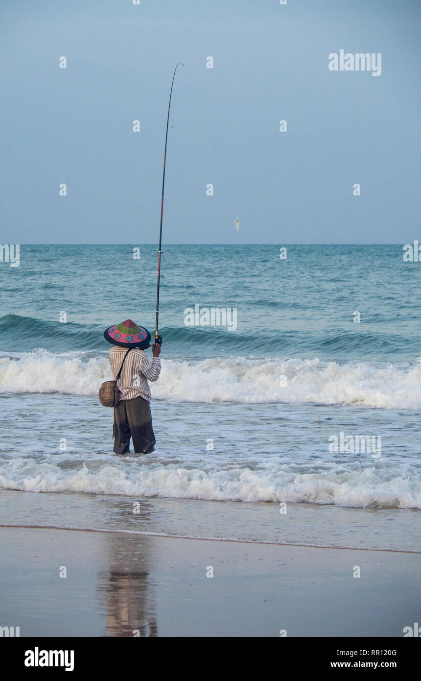 Pescatore solitario che indossa un cappello conico di pesca con un'asta fuori la spiaggia di Jimbaran Bay Bali Indonesia. Foto Stock