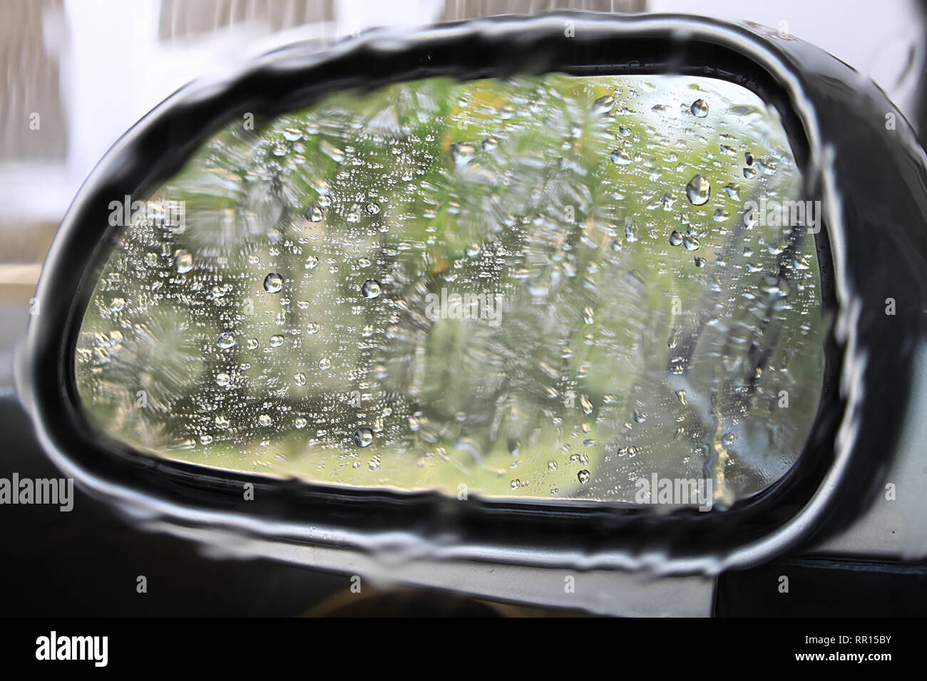 Un auto specchietto retrovisore coperto con acqua di pioggia cadute e la loro riflessione. Foto Stock