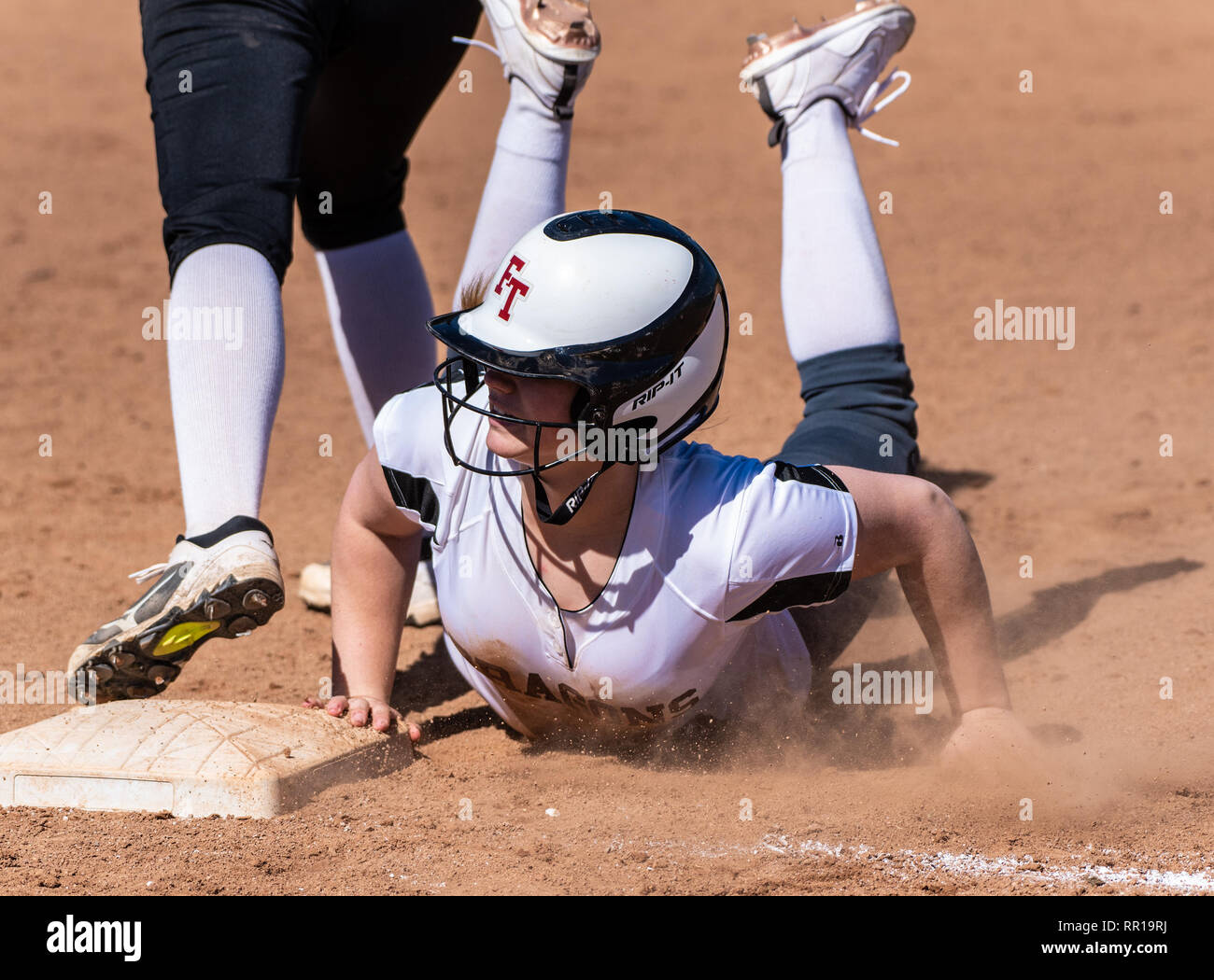 Softball player in bianco uniforme diving torna alla prima base nella nuvola di polvere durante il gioco tra la tecnologia Foothill High School e Pioneer Valley su Foto Stock