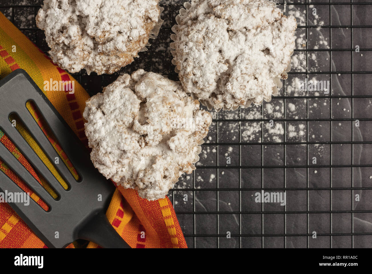 Tre cannella mollica muffin e un arancio brillante igienico con una spatola su una cremagliera con zucchero a velo sul marmo nero il ripiano del bancone Foto Stock