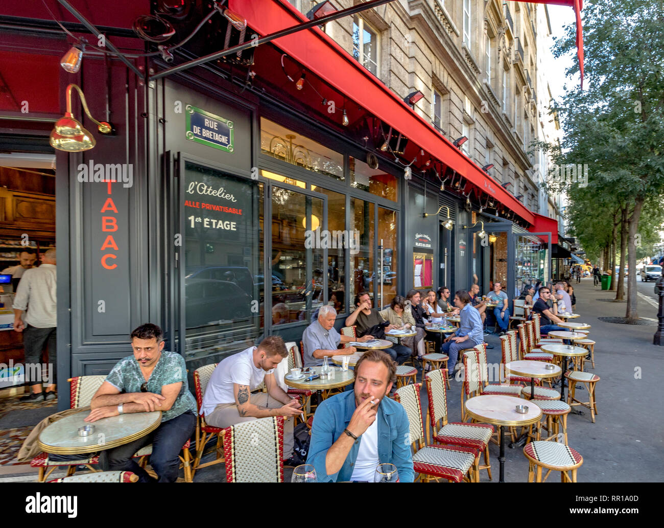 Un uomo che fuma una sigaretta seduta fuori sul marciapiede in un bar ristorante in Rue de Bretagne, Parigi, Francia Foto Stock