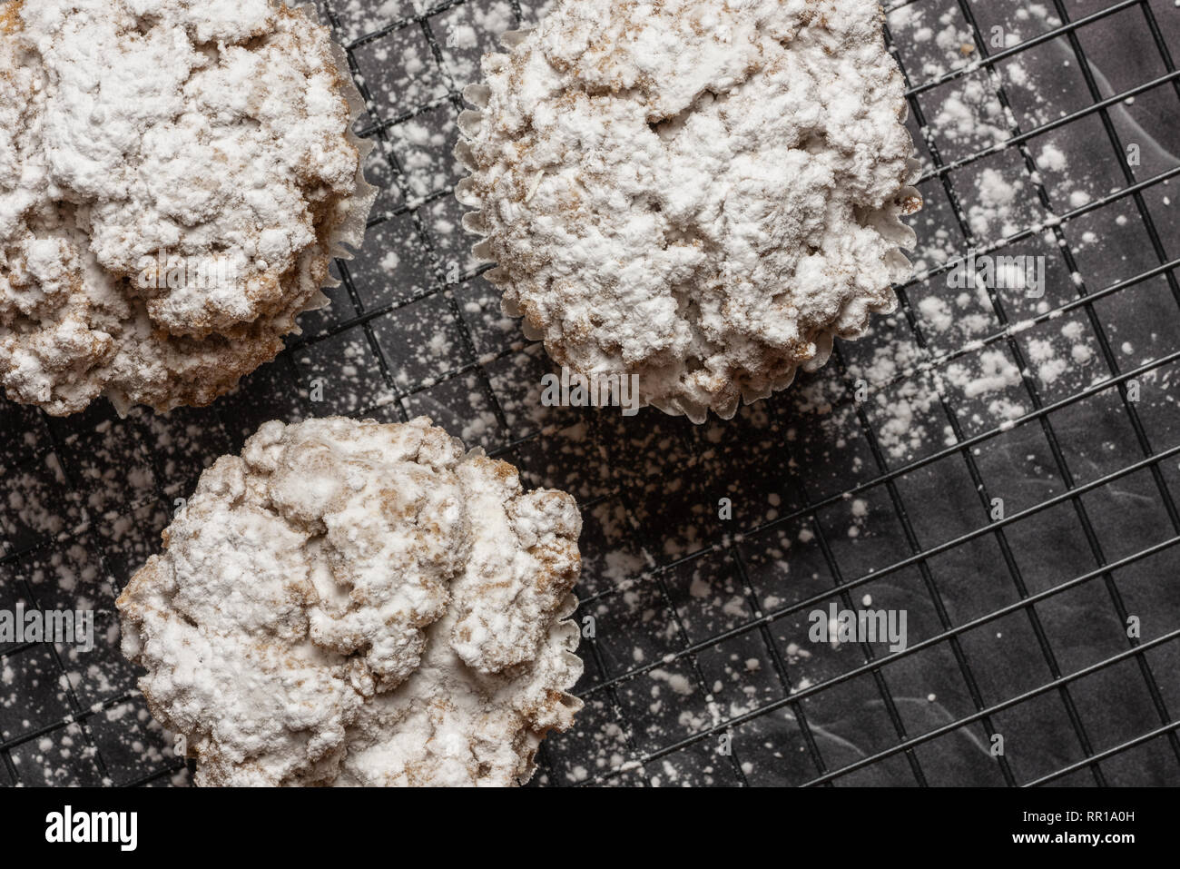 Tre cannella mollica muffin sulla diagonale su un rack con lo zucchero in polvere sul marmo nero il ripiano del bancone Foto Stock