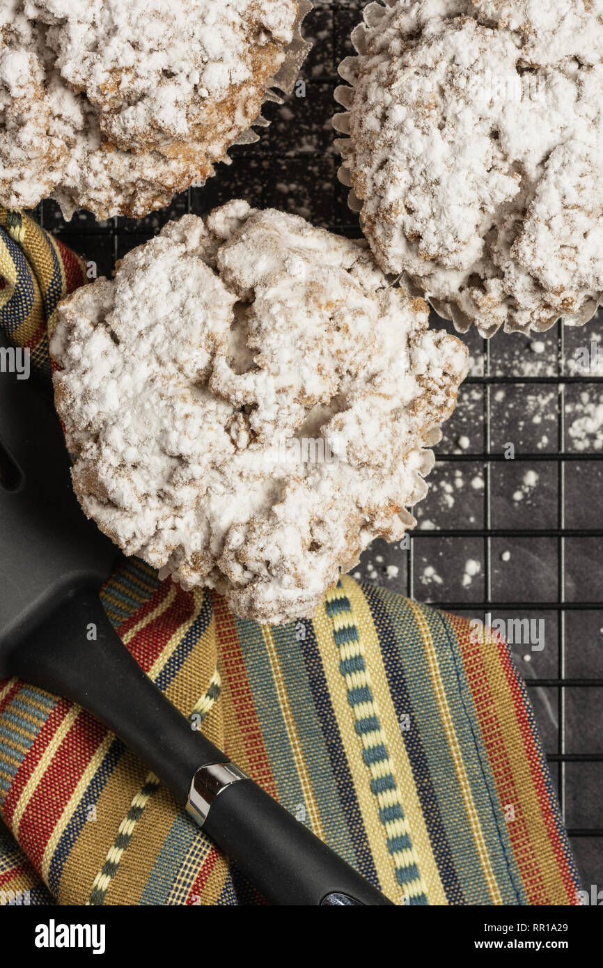 Tre cannella mollica muffin e tenui colori tovagliolo stripe con spatola su una cremagliera con zucchero a velo sul marmo nero verticale da banco Foto Stock