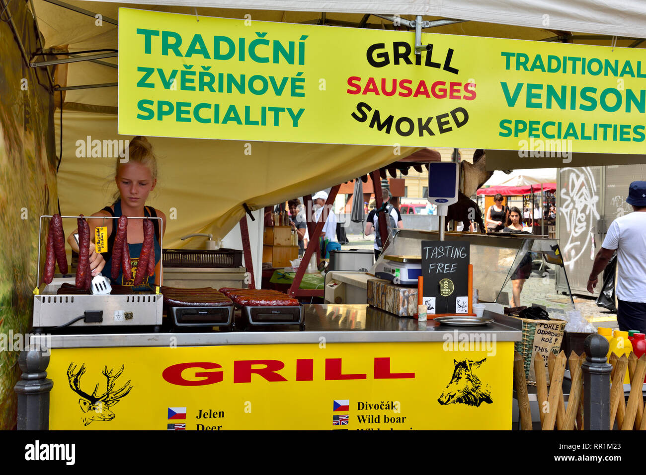 Giovane donna vendita stallholder tradizionali grigliate di salsicce di selvaggina al Mercato degli Agricoltori, Praga, Repubblica Ceca Foto Stock