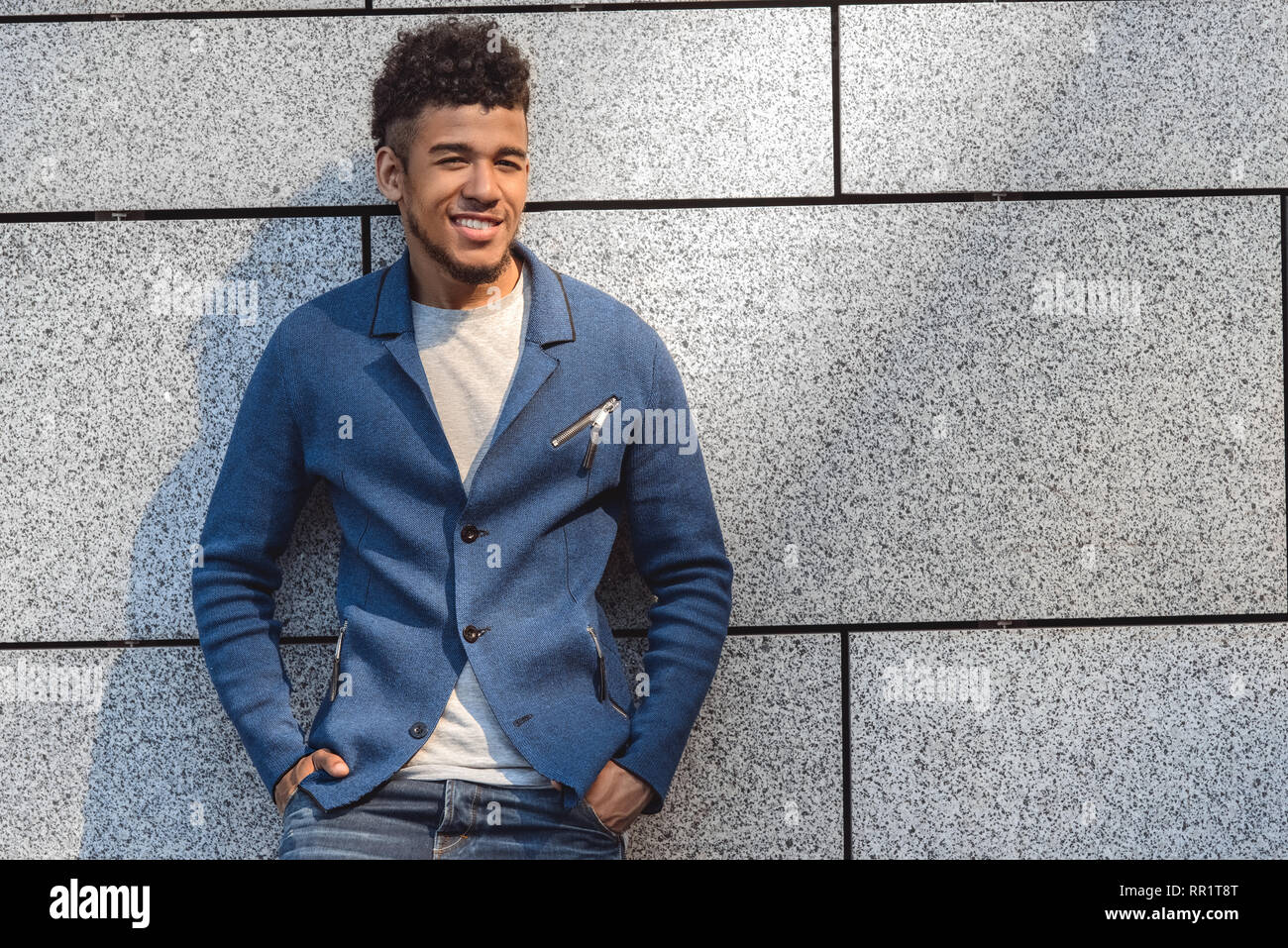 Freestyle. Mulatto guy standing isolato sulla parete mani nelle tasche sorridendo giocoso Foto Stock