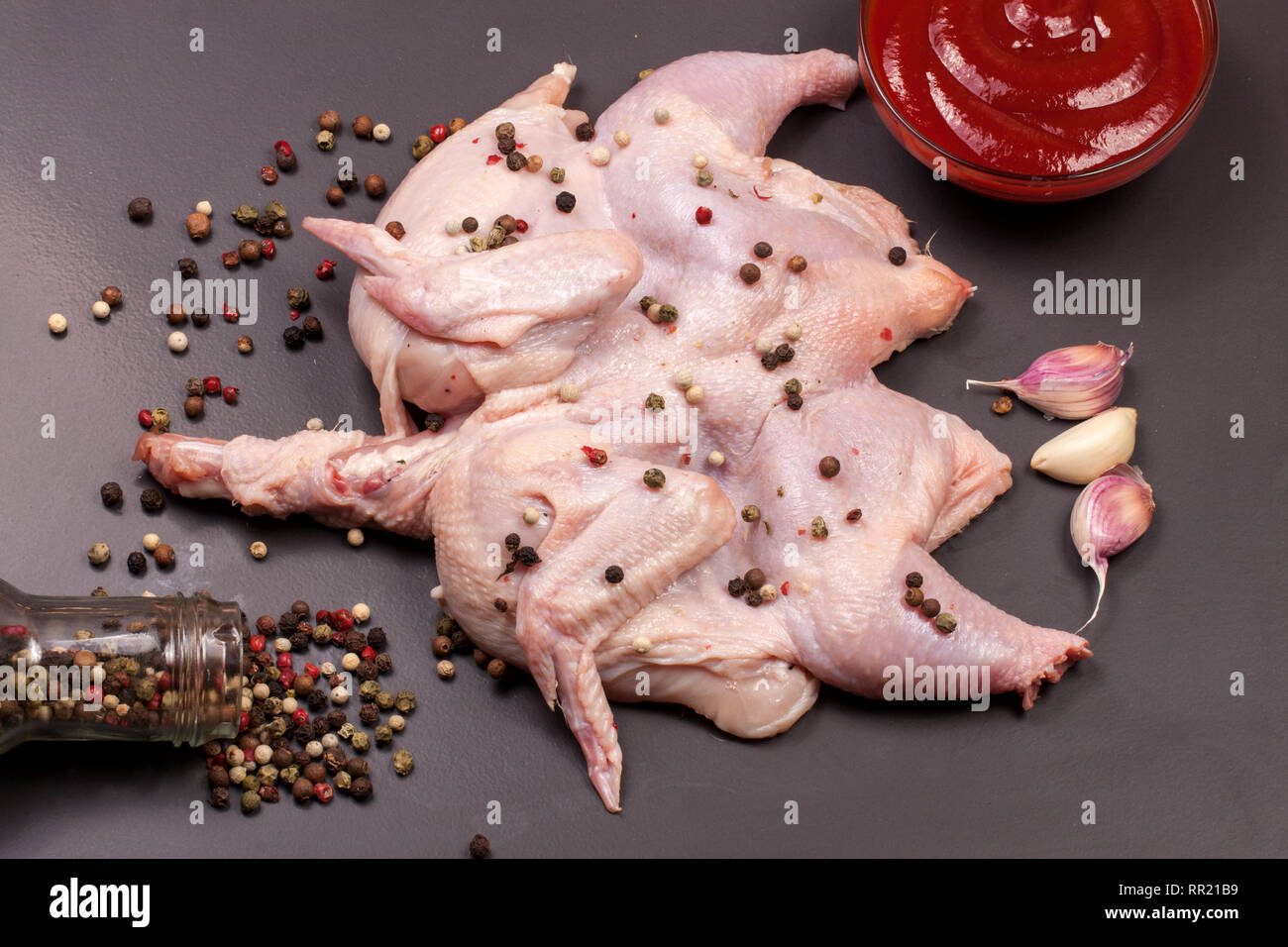 Il pollo crudo carcassa con chicchi di pepe nero su sfondo scuro Foto Stock