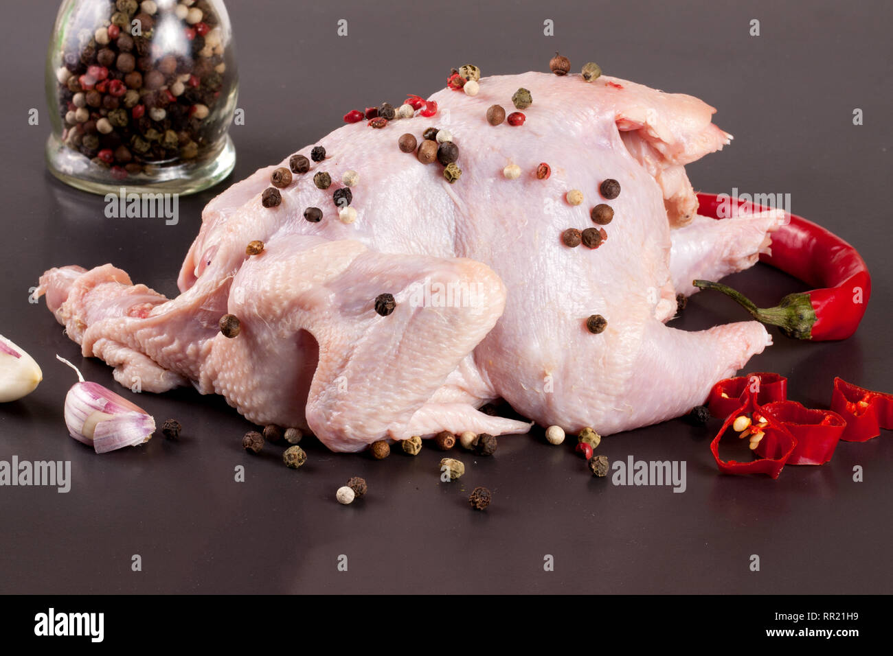 Il pollo crudo carcassa con chicchi di pepe nero su sfondo scuro Foto Stock