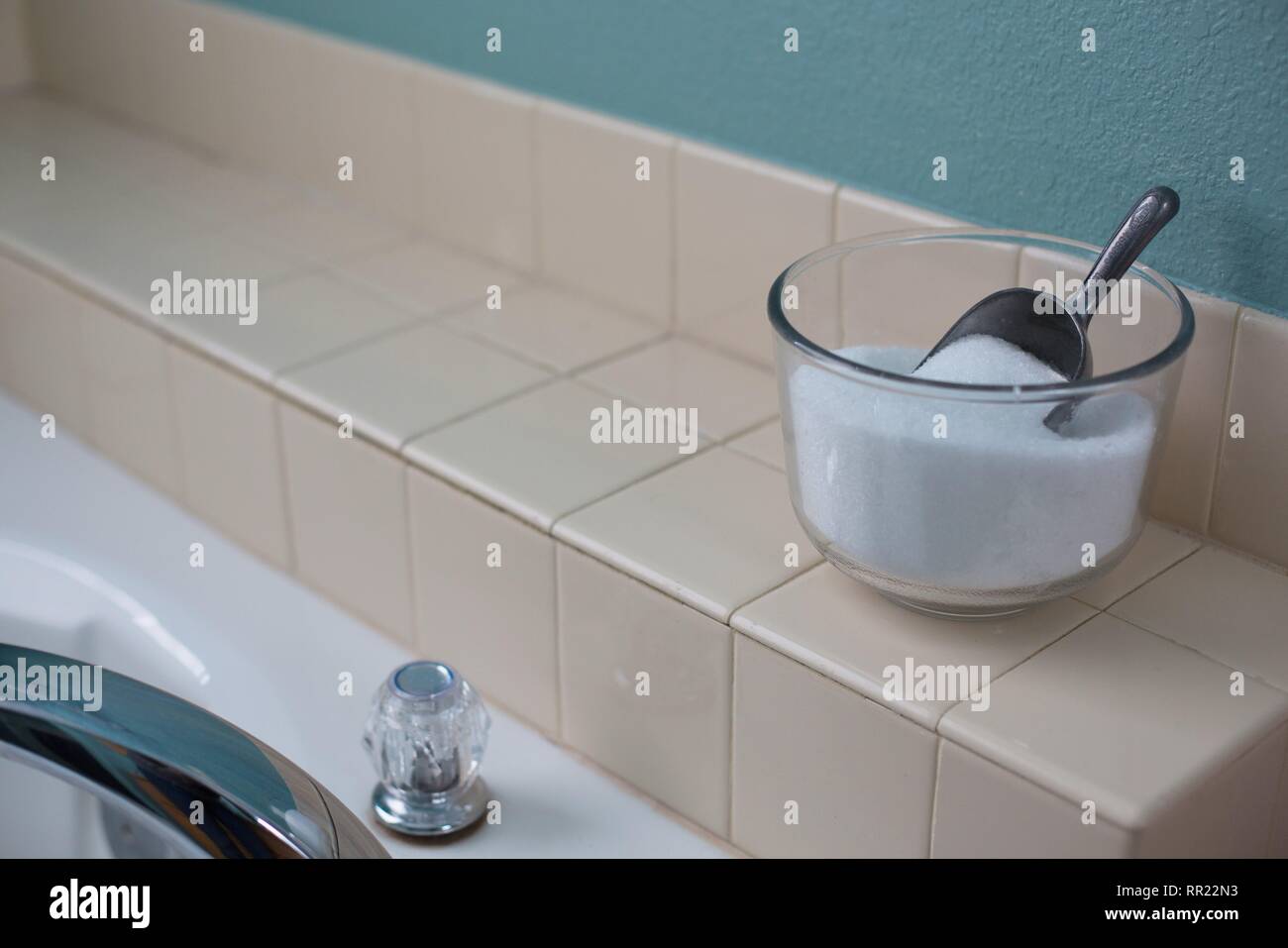 Una ciotola di sali di epsom con un cucchiaio, accanto a una vasca da bagno. Foto Stock