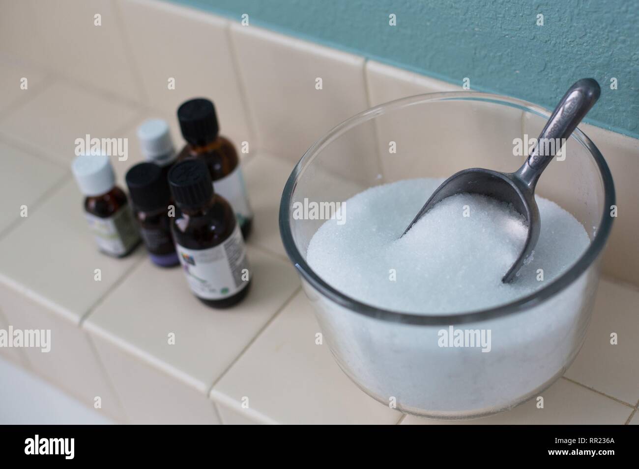 Una ciotola di sali di epsom con un cucchiaio e oli essenziali, accanto a una vasca da bagno. Foto Stock