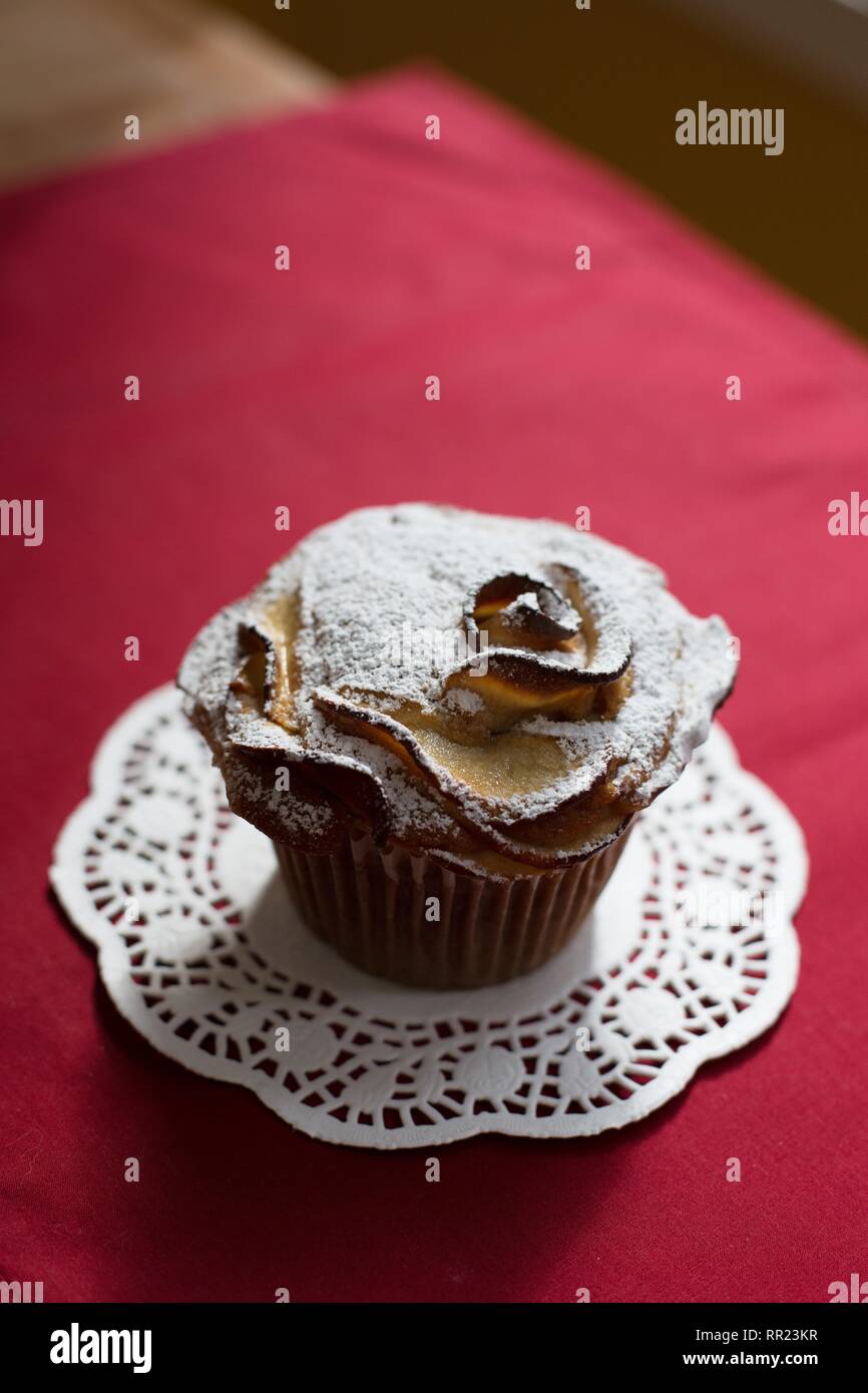 Un unico vegan muffin apple spolverato di zucchero a velo, su un centrino e tovaglia rosso. Foto Stock