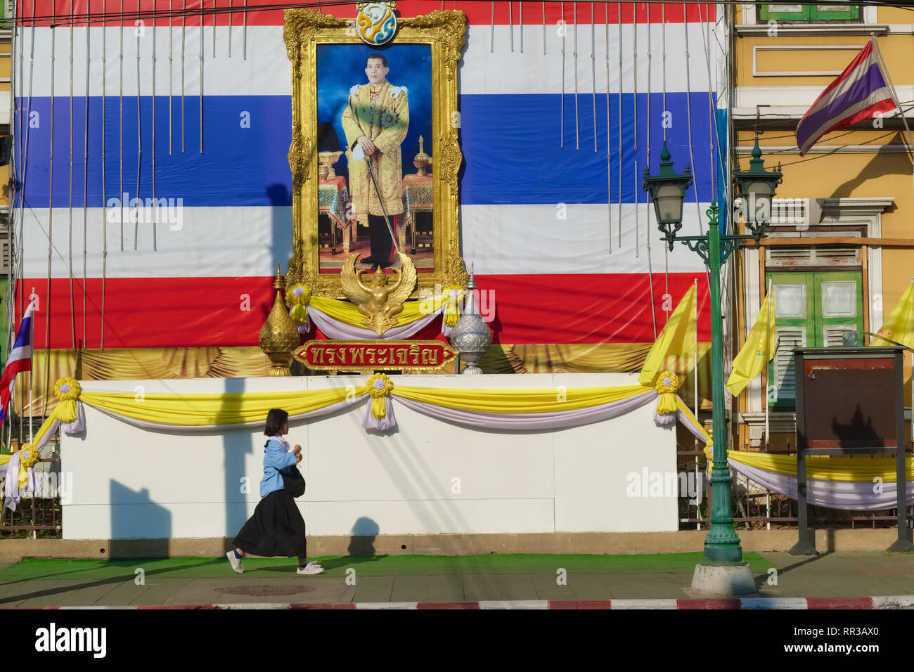 Un schoolgirl a Bangkok, Thailandia, passa sotto un ritratto di Re Maha Vajiralongkorn, Rama X., impostare contro un gigante bandiera tailandese Foto Stock