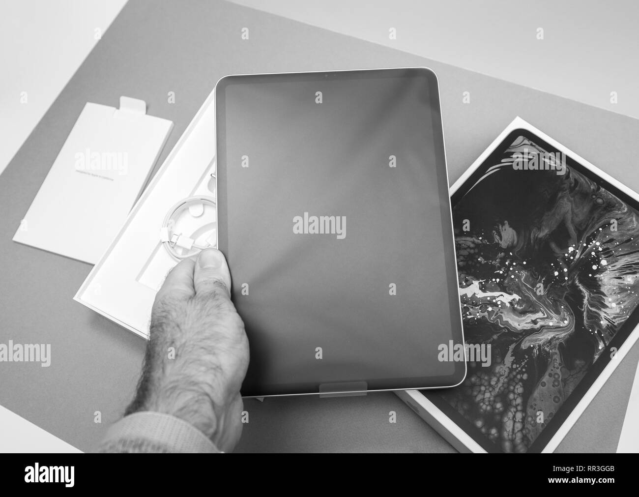 Parigi, Francia - 14 NOV 2018: Man mano che tiene il disimballaggio Disimballaggio del nuovo iPad Pro dal computer Apple tablet in office tabella nel verde di colore bianco - compressa ancora nella protezione di plastica Pellicola in bianco e nero Foto Stock
