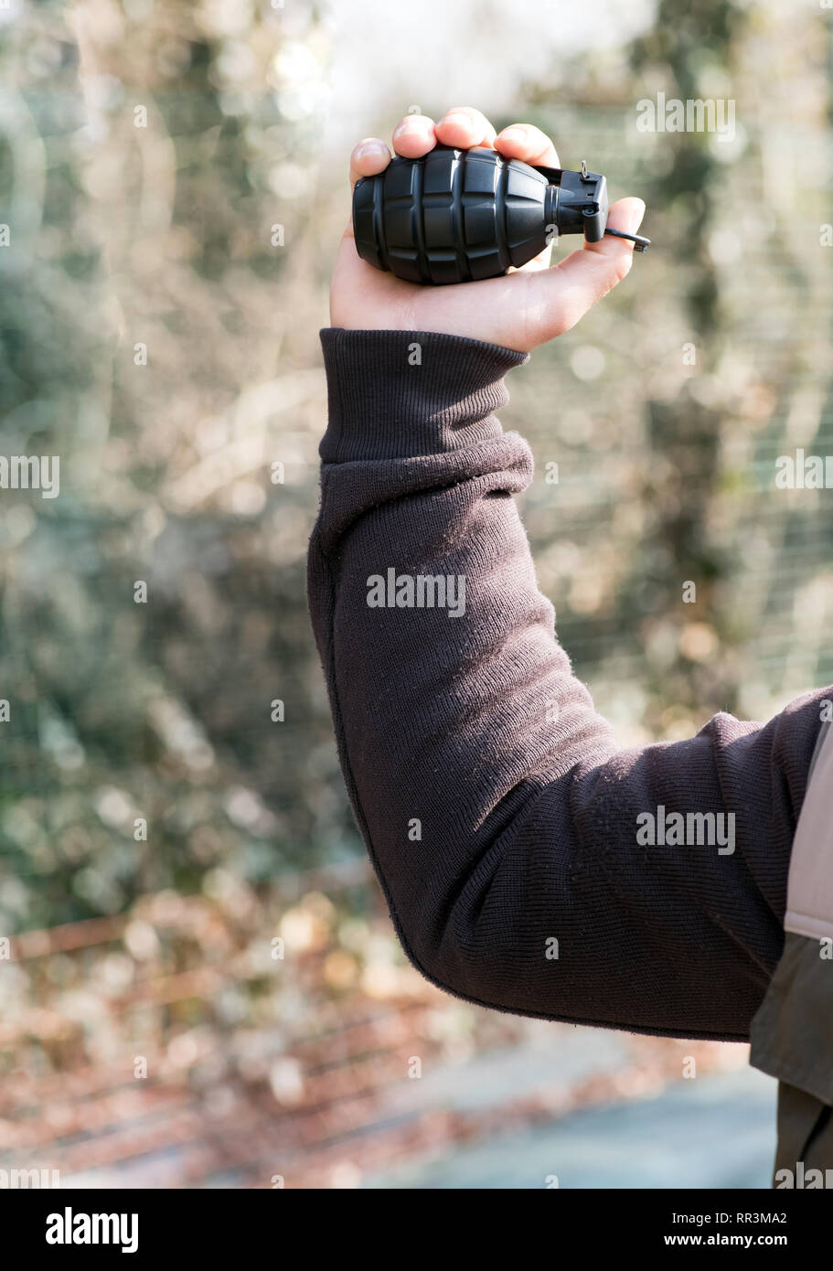 Uomo in posa per lanciare una granata alzando la mano in aria con l'anello del perno agganciato sul suo pollice in un concetto di guerra o di terrorismo Foto Stock