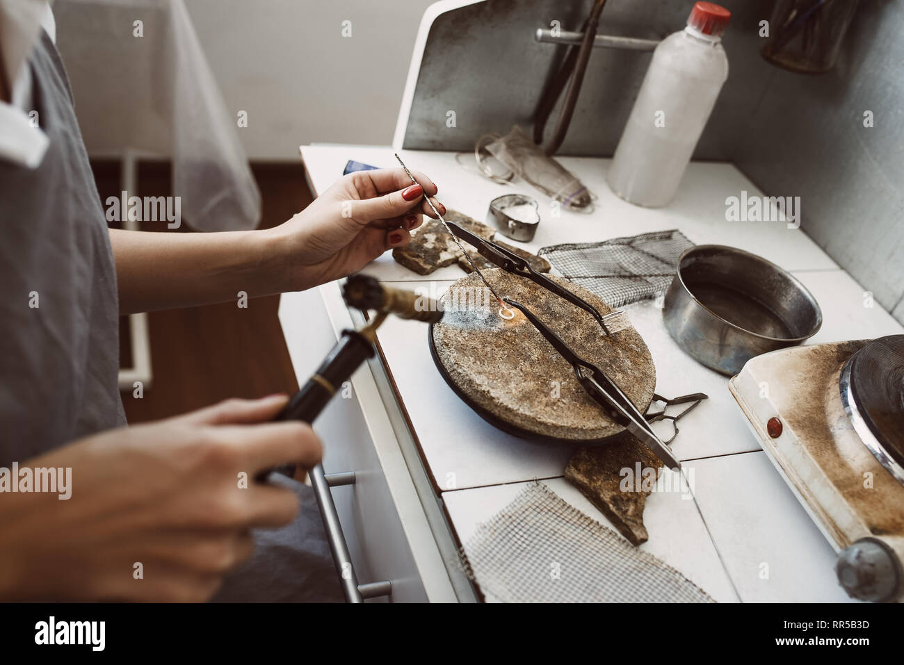 Delicato lavoro. Vista laterale del gioielliere le mani la saldatura un argento orecchini con fiamma dalla torcia di saldatura in corrispondenza di gioielleria workshop. Foto Stock