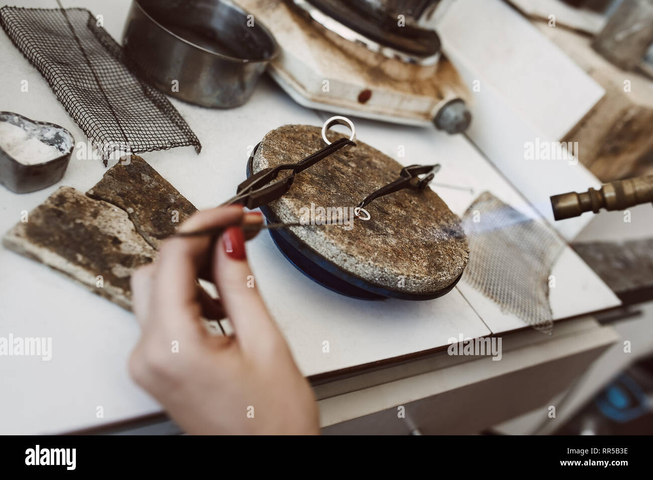 Lavoro pericolose. Vista superiore del gioielliere le mani la saldatura un argento orecchini con fiamma dalla torcia di saldatura in corrispondenza di gioielleria workshop. Foto Stock