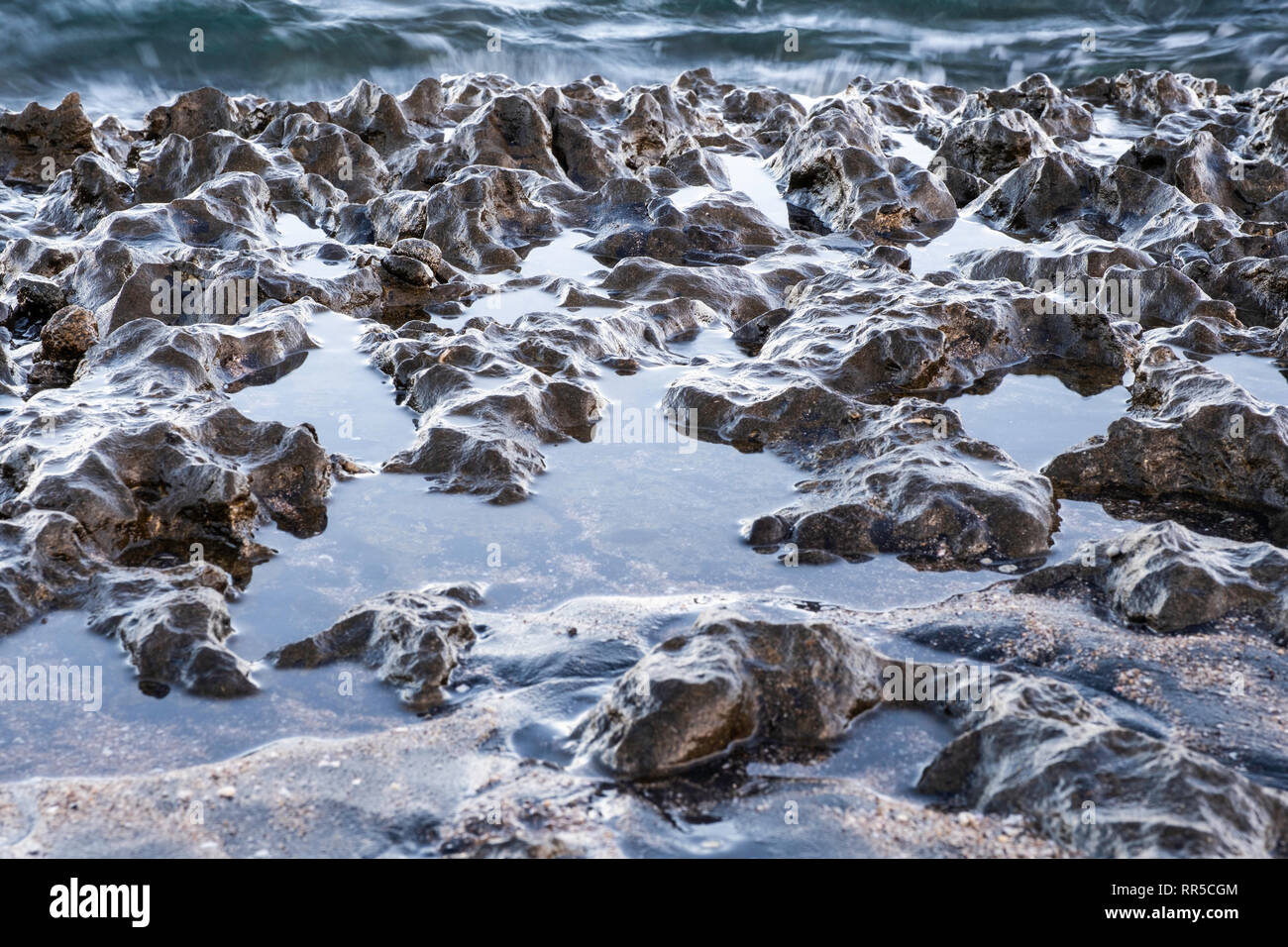 Come le onde che si infrangono sulla roccia vulcanica sulla Playa Ocotal e in Costa Rica, l'acqua lascia le rocce scintillanti di bagnato con la comparsa di una montagna ra Foto Stock
