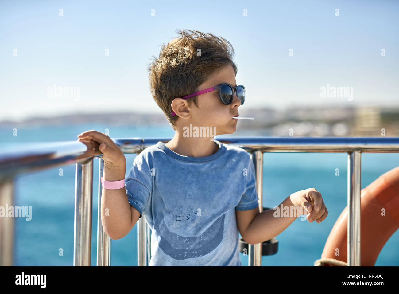 Piccolo Ragazzo in occhiali da sole di mangiare lecca-lecca sul ponte dello yacht Foto Stock