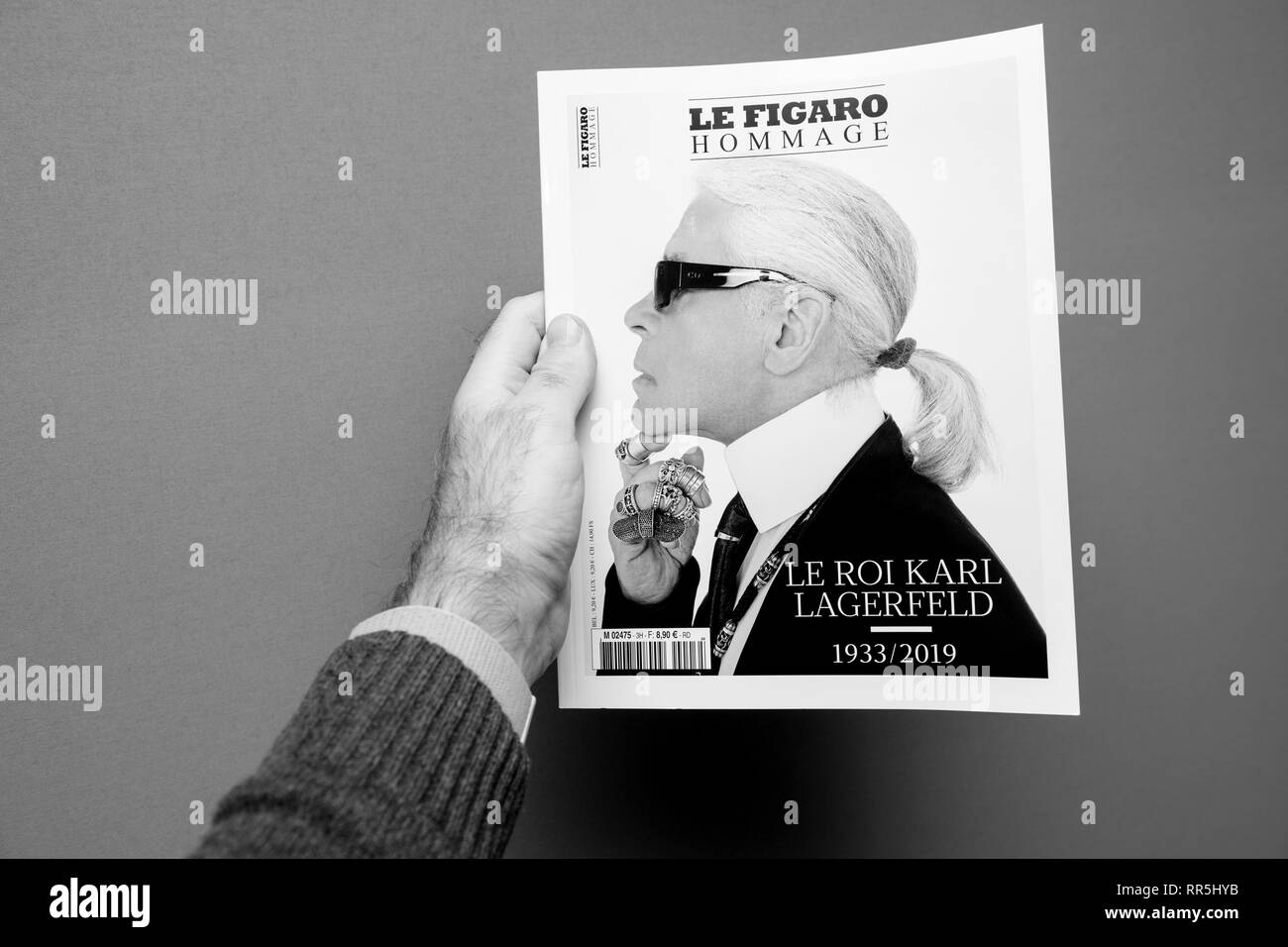 Parigi, Francia - Feb 23, 2019: l'uomo che mostra il francese Le Figaro hommage rivista omaggio a copertura di Karl Lagerfeld morte, iconico designer di moda sono morti di età compresa tra i 85 - isolato sfondo grigio - bianco e nero Foto Stock