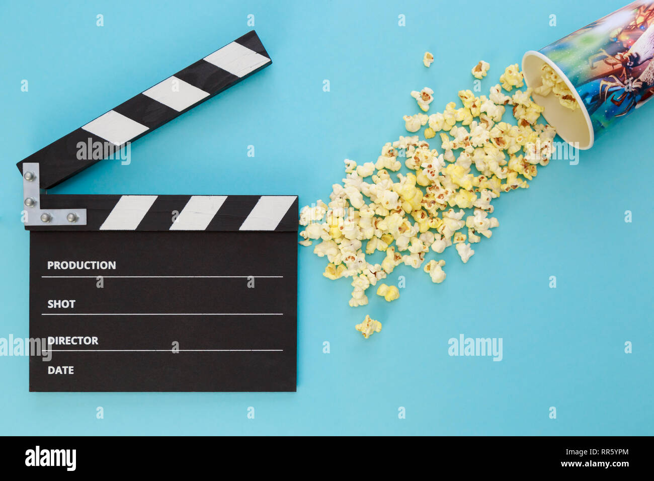 Clapperboard nero e una tazza con popcorn sparsi su uno sfondo blu Foto Stock