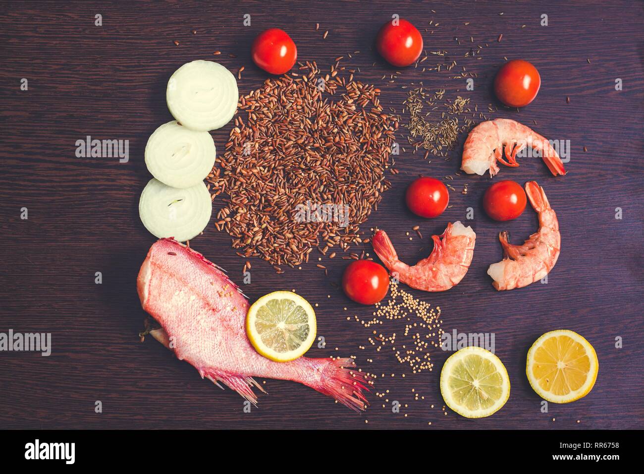 Ingredienti per la cucina indiana sono su un nero superficie di legno. La composizione del piatto include pesce cernia, spicchi di limone, un trito di cipolla, marrone r Foto Stock