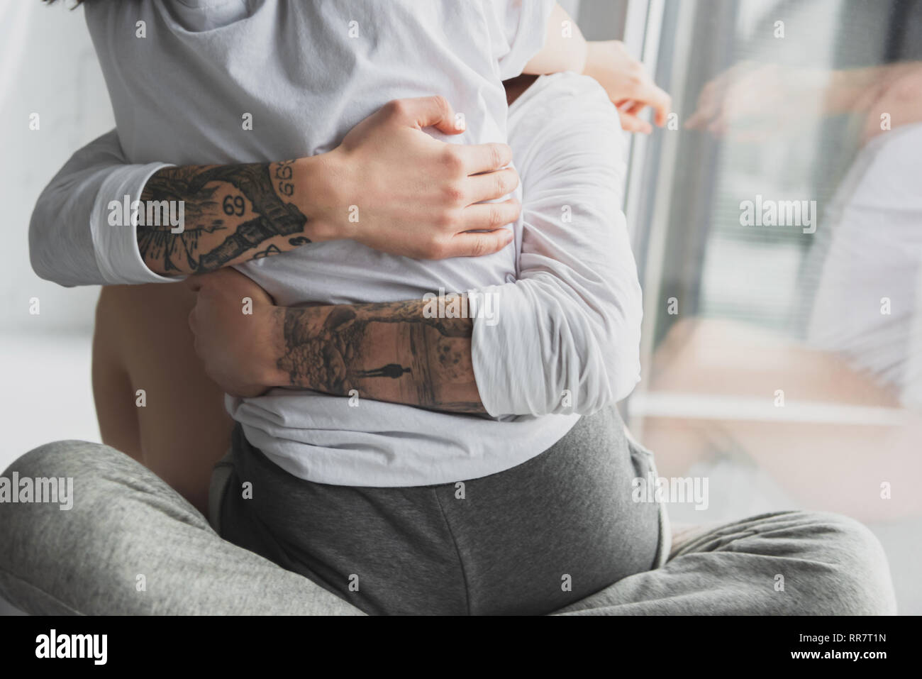 Vista ritagliata della tatuato uomo appassionatamente abbracciando la donna a casa Foto Stock