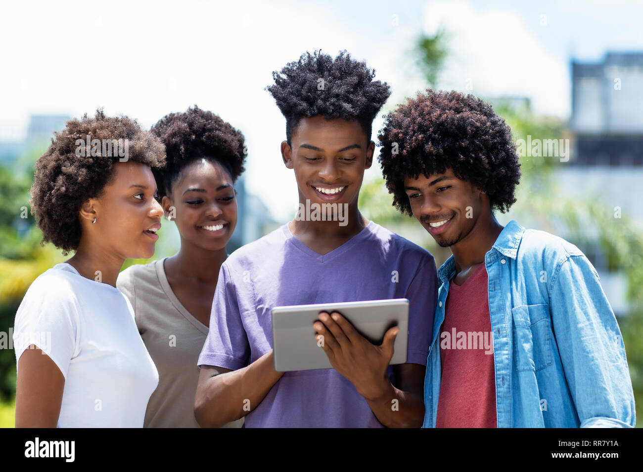 Gruppo di afro-americano di giovani adulti inviare messaggio con tavoletta digitale all'aperto in estate Foto Stock