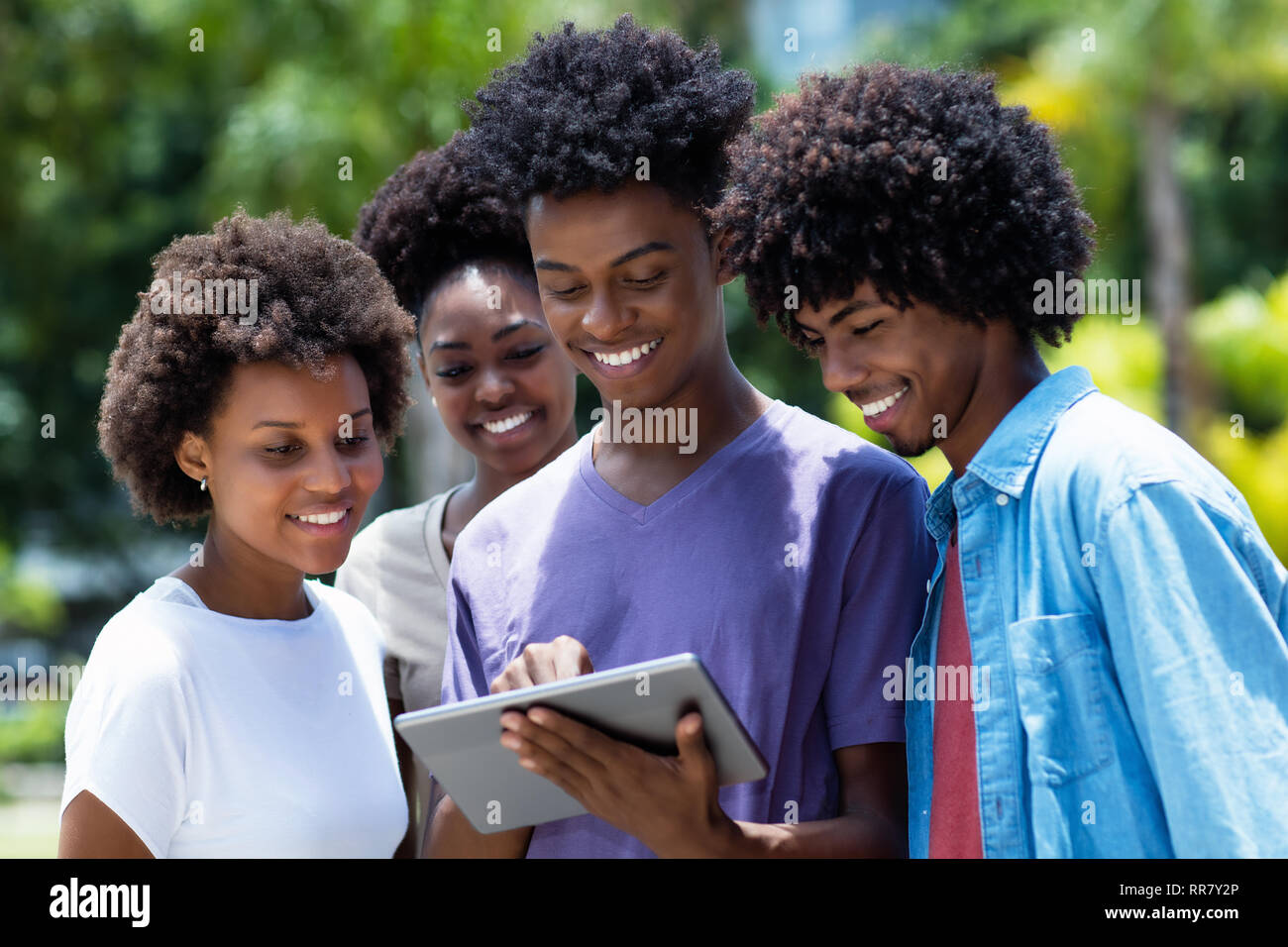 Gruppo di afro-americano di giovani adulti guardando film con tavoletta digitale all'aperto in estate Foto Stock