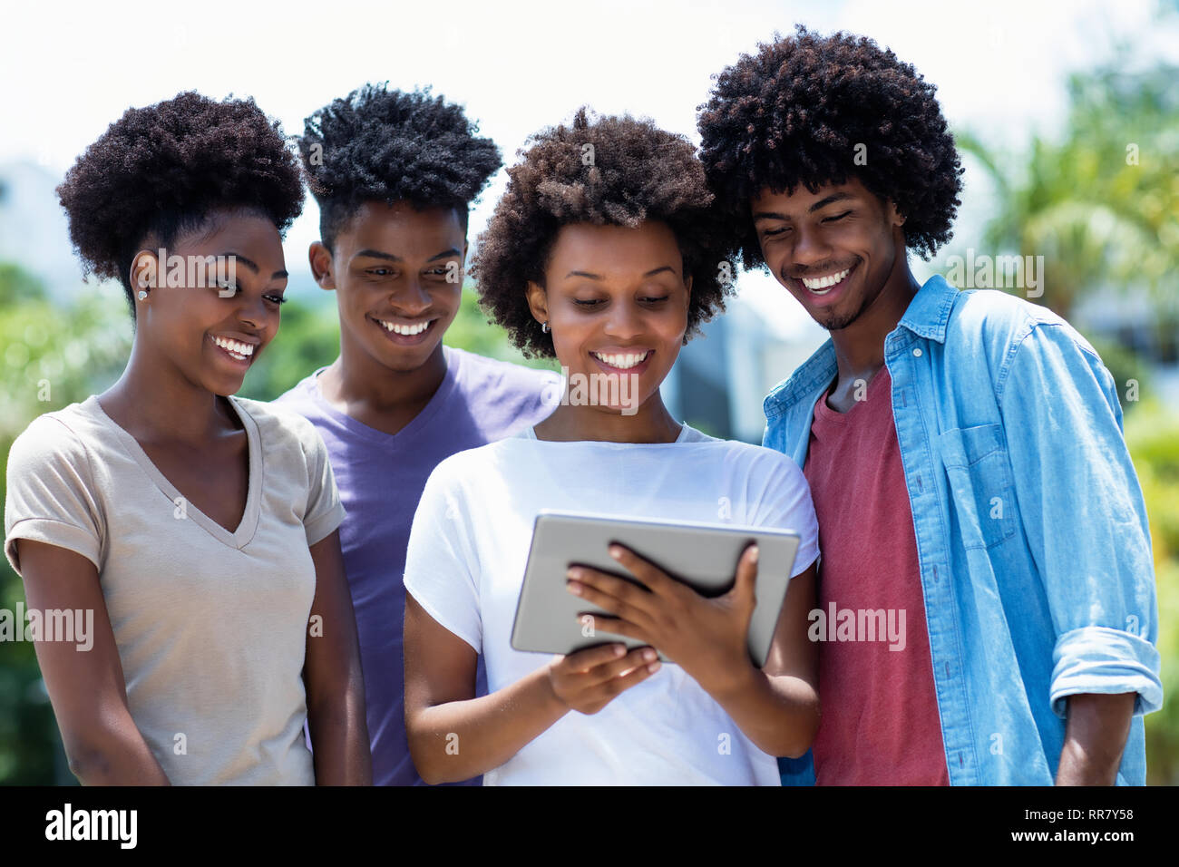 Gruppo di afro-americano di giovani adulti la lettura di notizie con tavoletta digitale all'aperto in estate Foto Stock