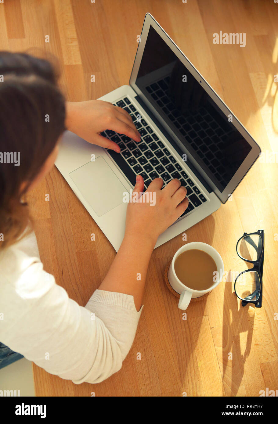 Vista dall'alto di womans mani digitando sulla tastiera del notebook con gli occhiali e il caffè sul tavolo. Mock up minimo piatto eroe laico la testata Foto Stock