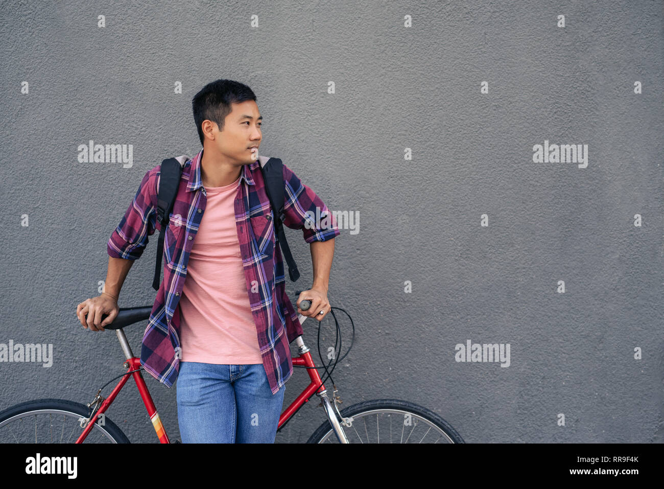 Giovane uomo pendente con la sua moto contro un muro grigio Foto Stock