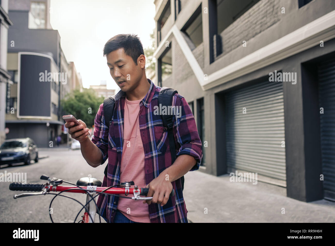 Giovane uomo asiatico a piedi con la sua bicicletta utilizzando un telefono cellulare Foto Stock