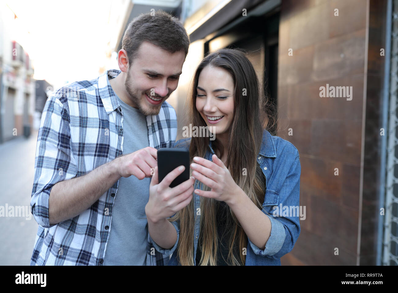 Due happy amici o di coppia utilizzando un telefono intelligente a piedi in strada Foto Stock