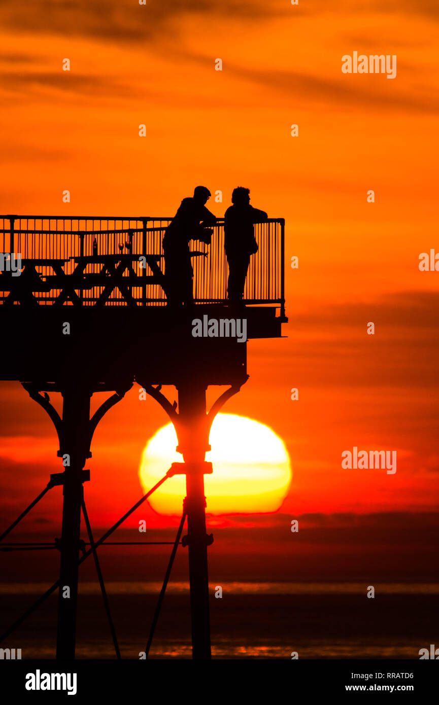 Aberystwyth Ceredigion Wales UK, lunedì 25 febbraio 2019. Regno Unito: Meteo il sole tramonta drammaticamente dietro le persone in piedi sul molo di Aberystwyth alla fine di una giornata o di registrare le temperature di rottura e ininterrotte di sole. Trawsgoed, a poche miglia di navigazione della città, registrati 20.3º Celsius la temperatura più alta mai recored nel Regno Unito nel mese di febbraio Photo credit Keith Morris/Alamy Live News Foto Stock