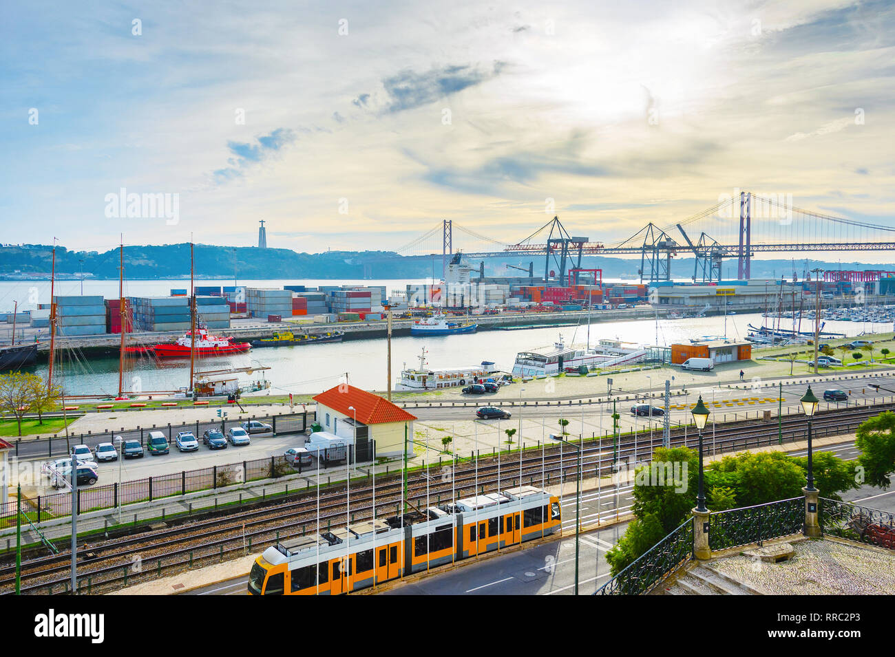 Treno della metropolitana passando per città commerciale porta con contenitori di carico e il trasporto di merci per le gru a ponte 25 Aprile, Cristo Re statua di Almada in backgrou Foto Stock