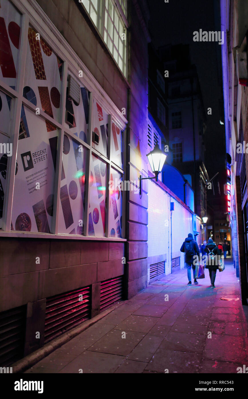 L uomo e la donna a piedi verso il basso trascinando allyway borse per lo shopping di notte, Londra, Inghilterra, Regno Unito Foto Stock