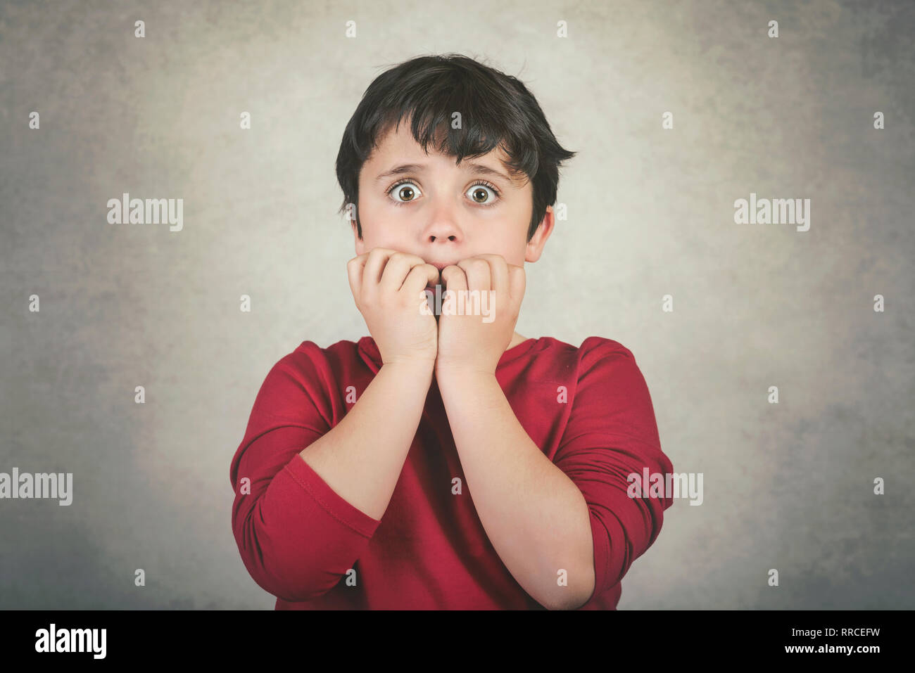 Scary kid che morde la sua le unghie contro uno sfondo grigio Foto Stock